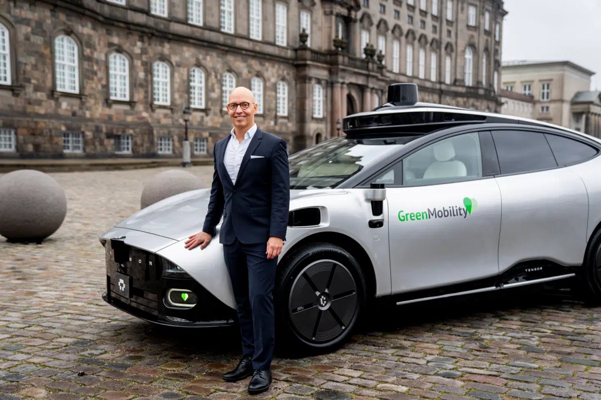A GreenMobility executive beside a silver Tensor Level 4 autonomous car in front of Christiansborg Palace, Copenhagen.
