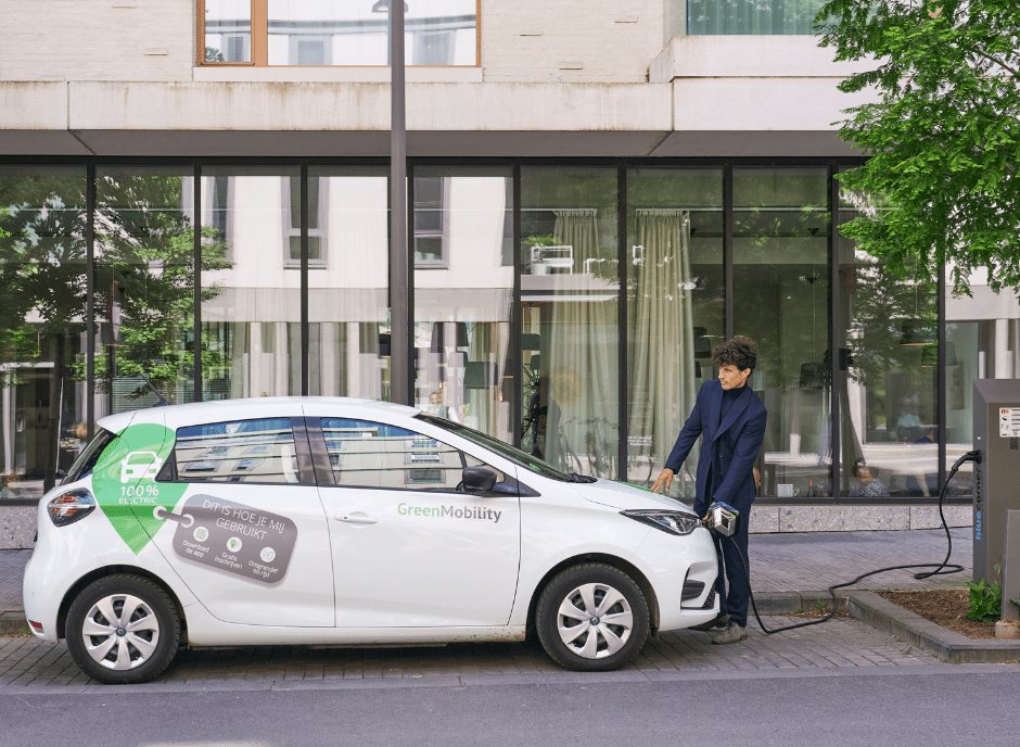 A driver plugging in a GreenMobility electric carsharing vehicle at a curbside charge point.