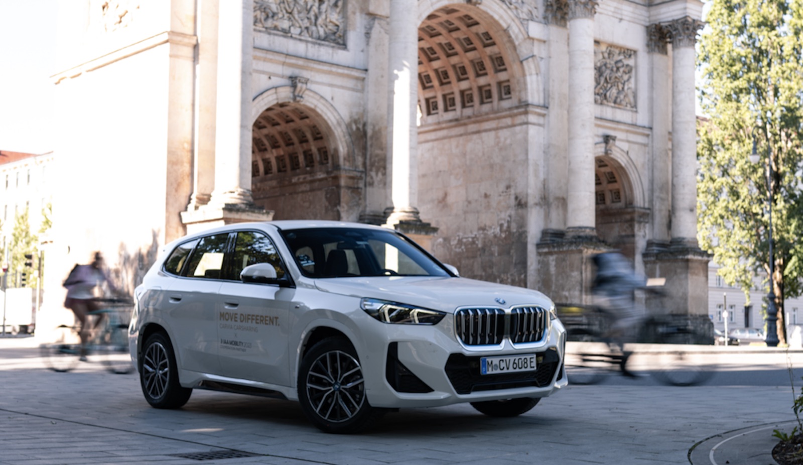 A white CarVia BMW electric SUV by the Siegestor arch in Munich