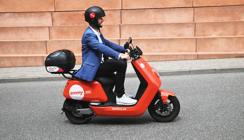 A rider on a red emmy shared e-moped on a city street